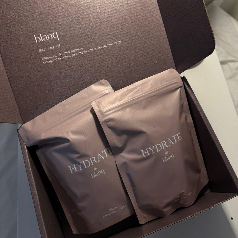 Two Blanq Hydrate pouches inside an open, dark brown Blanq gift box