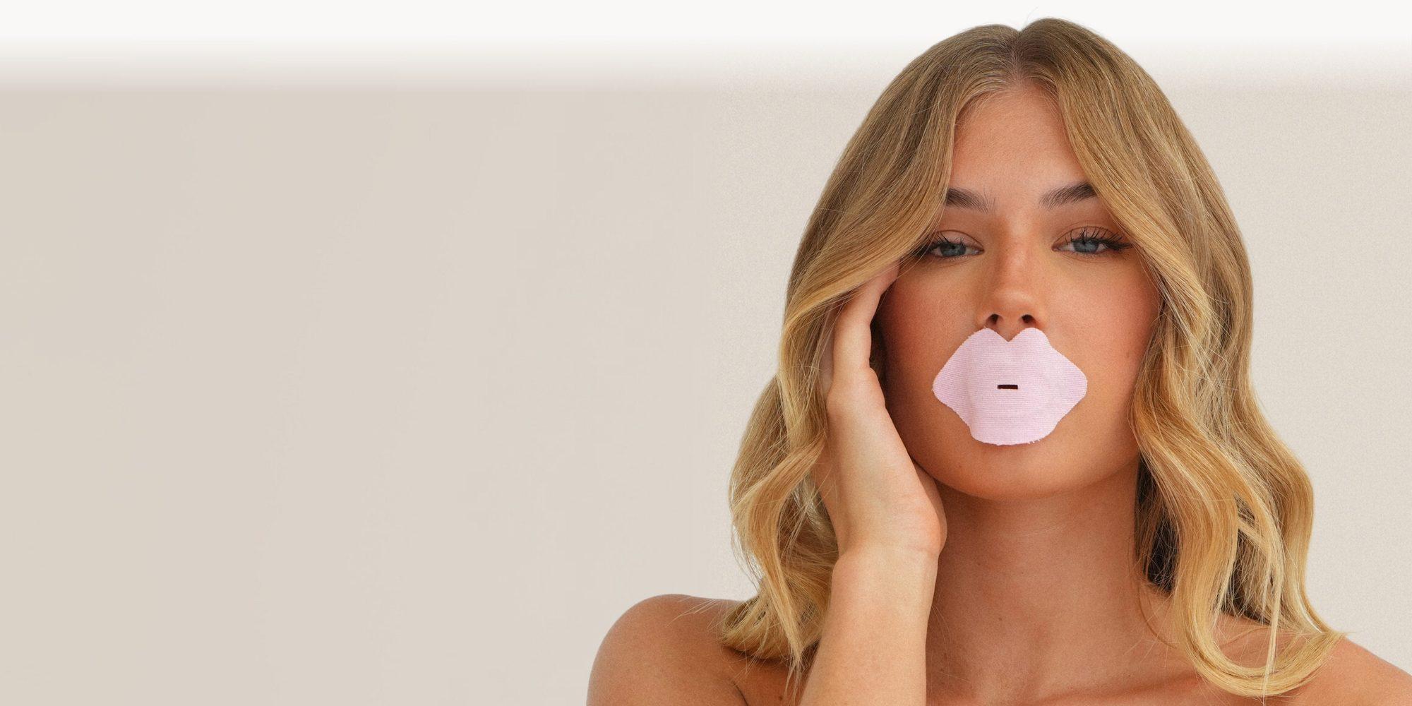 Model wearing pink Blanq Hydrate mouth tape, one hand resting against her face, on a soft neutral background