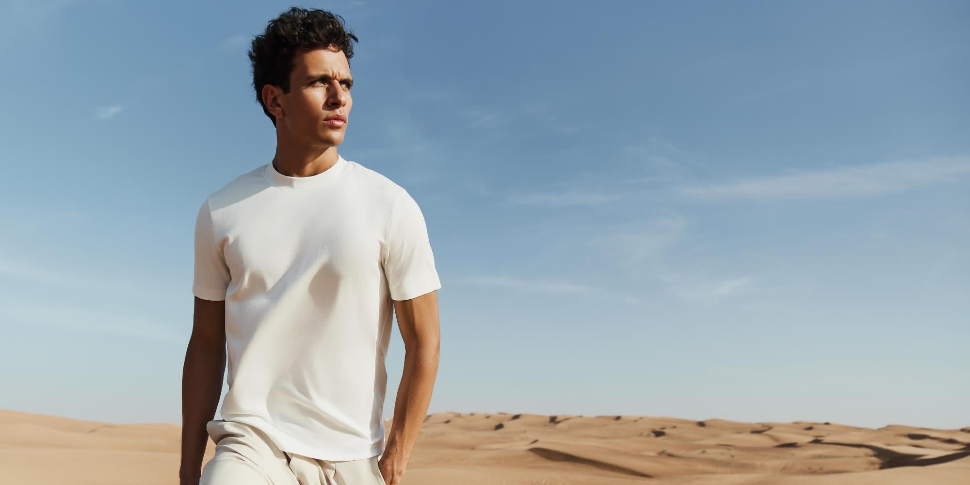 Model in a white Maen Donati tee and stone-coloured trousers walking across desert dunes under a clear sky