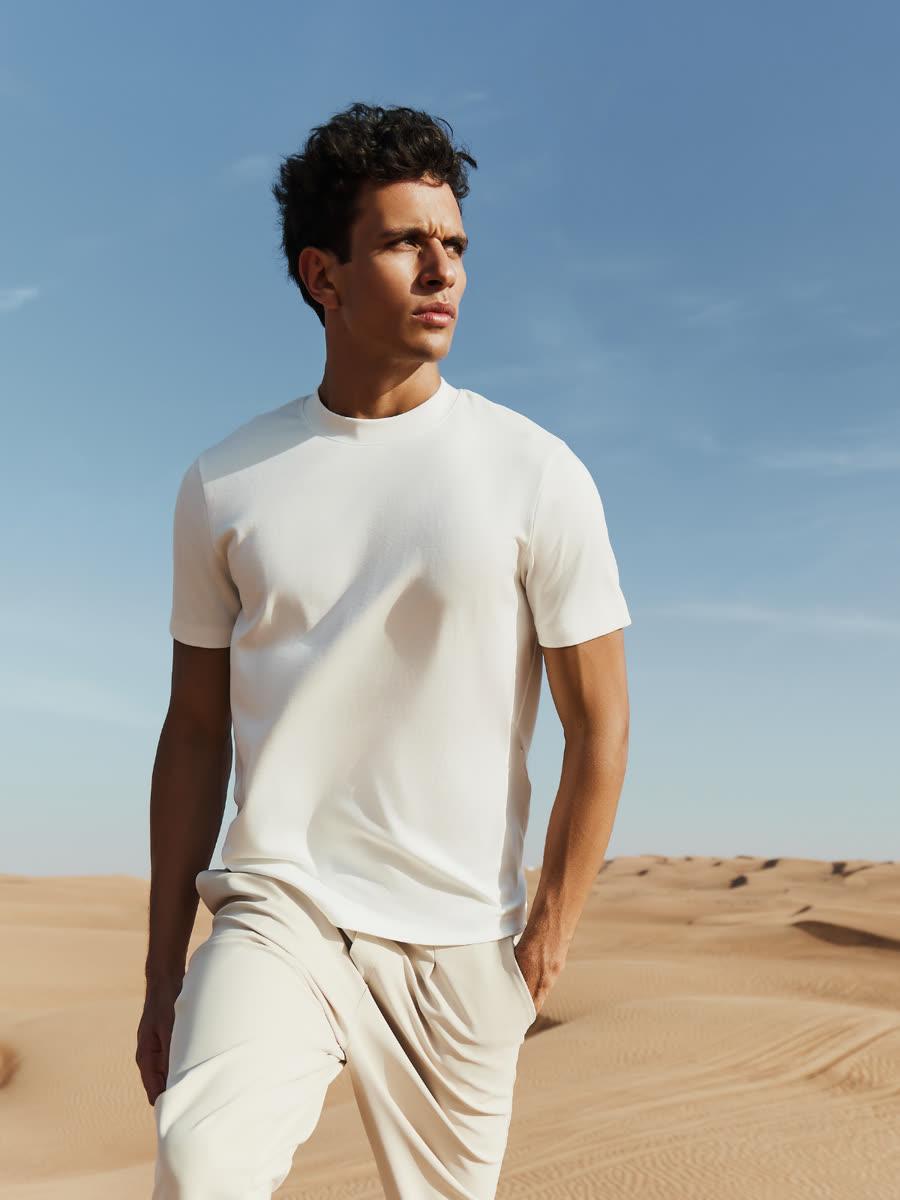 Model in a white Maen Donati tee and stone-coloured trousers standing in desert dunes